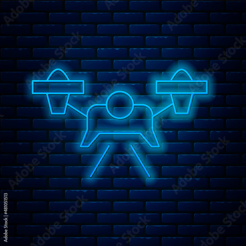 Glowing neon line Drone flying icon isolated on brick wall background. Quadrocopter with video and photo camera symbol. Vector