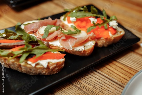 bruschetta with salmon, cottage cheese, dried tomatoes and micro greens, on a black background