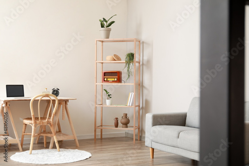 Interior of light room with modern workplace and shelving unit