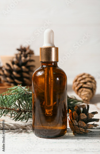 Bottle of essential oil, fir branch and pine cones on light wooden background, closeup