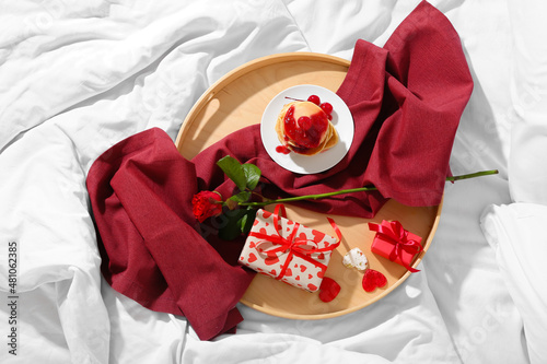 Tray with delicious breakfast and presents for Valentine's Day on soft bed