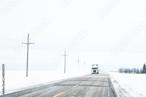 Oncoming eighteen-wheeler on a highway drifting with snow in a countryside winter landscape