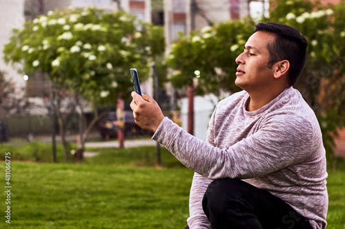 revisando su trabajo en su celular esta un joven latino mientras toma un pausa de sus labores en un parque de la cuidad
