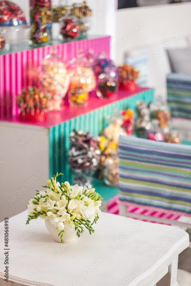 Centerpiece with flowers in the foreground. In the background shelves with sweets, candy bar Style. festive setting