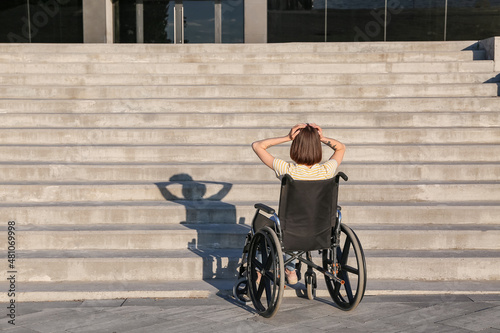 Stressed young woman in wheelchair near stairs outdoors photo