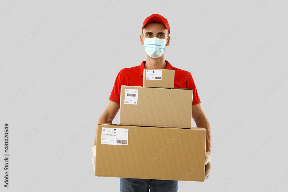 Fototapeta premium Male courier in medical mask and with parcels on light background