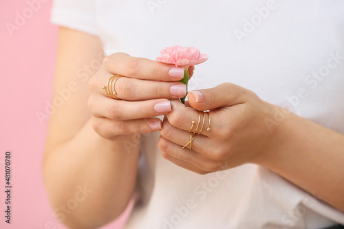 Woman with beautiful manicure and stylish jewelry holding beautiful carnation flower on color background