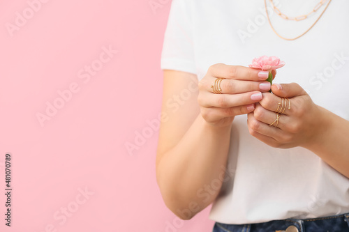 Woman with beautiful manicure and stylish jewelry holding carnation flower on color background