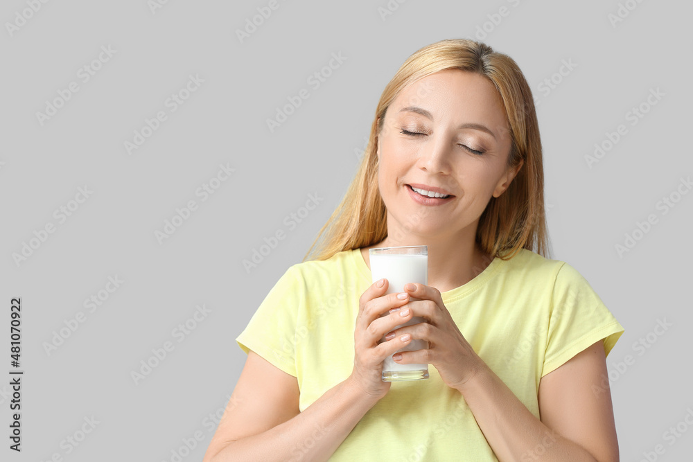 Mature woman with glass of milk on grey background Mature woman with glass of milk on grey background