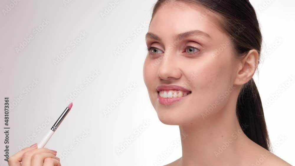 Girl paints her lips with a lip brush. Caucasian model doing make-up. Woman makes makeup. Cosmetic and Skin care concept. Natural healthy face. Beauty treatment on white isolate background. Girl paints her lips with a lip brush. Caucasian model doing make-up. Woman makes makeup. Cosmetic and Skin care concept. Natural healthy face. Beauty treatment on white isolate background.