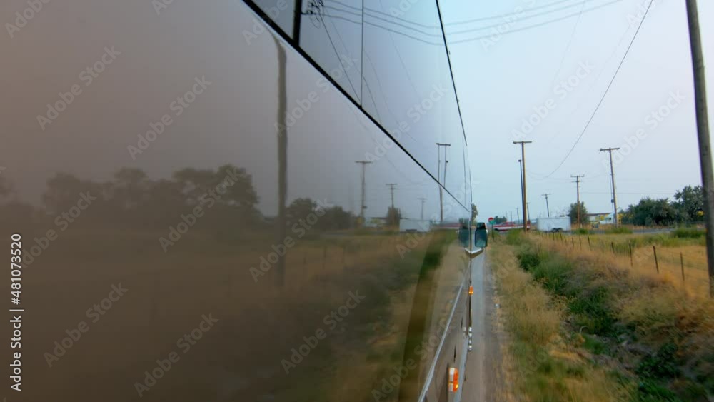 Side view of a public bus, shuttle, or school bus driving and the road reflection on it. Driving on the edge of a country road passing a warning stop sign and stopping at a stop sign and turning left. Side view of a public bus, shuttle, or school bus driving and the road reflection on it. Driving on the edge of a country road passing a warning stop sign and stopping at a stop sign and turning left.