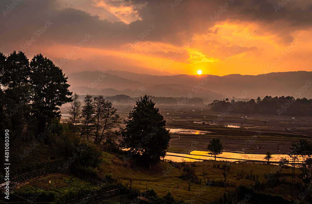 Obraz premium sunrise over mountains with country side farming fields and orange dramatic sky at dawn at village