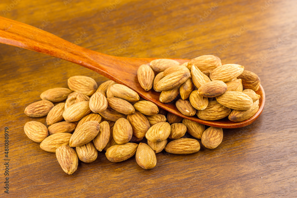 Almonds seeds pour from wood spoon on textured wooden background, top view.