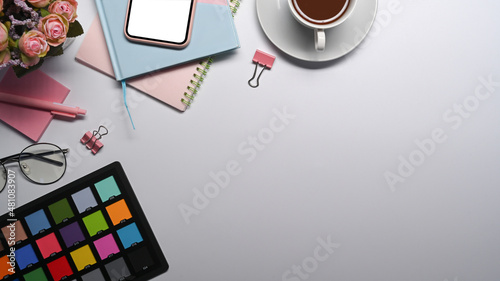 Graphic designer workplace, color swatch, coffee cup, notebook and smart phone on white table.