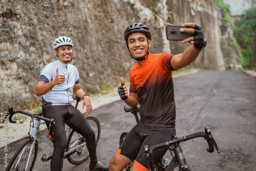 Obraz premium male cyclist sitting on bike and using phone to take selfie or video calling