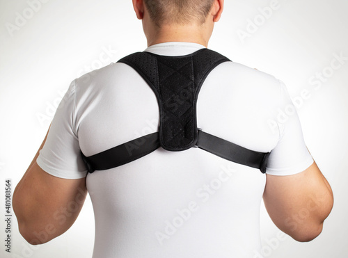 A man in a white T-shirt with a black posture corrector on a white background. Back pain and problem correction concept, treatment photo
