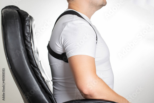 A male is wearing an orthopedic posture corrector. Treatment for stoop and back problems, close-up. The guy sits on a chair in the office photo