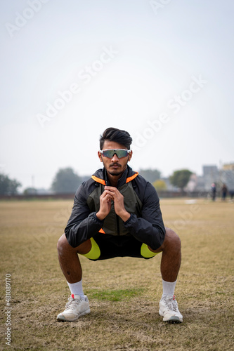 Front shot of an indian boy doing squats in the field wearing sports outfit. Sports and lifestyle concept.