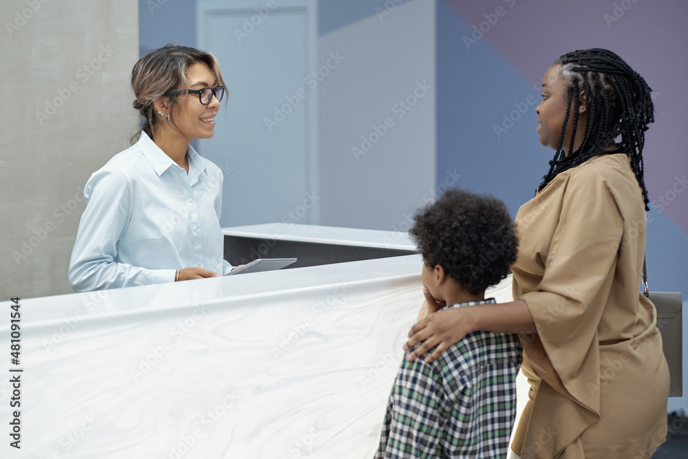 Friendly receptionist consulting young African woman with son going to make appointment with dentist