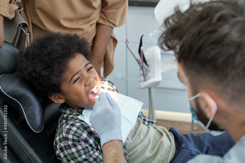 Little African boy with open mouth having oral check-up while sitting in armchair in contemporary dental clinics Little African boy with open mouth having oral check-up while sitting in armchair in contemporary dental clinics