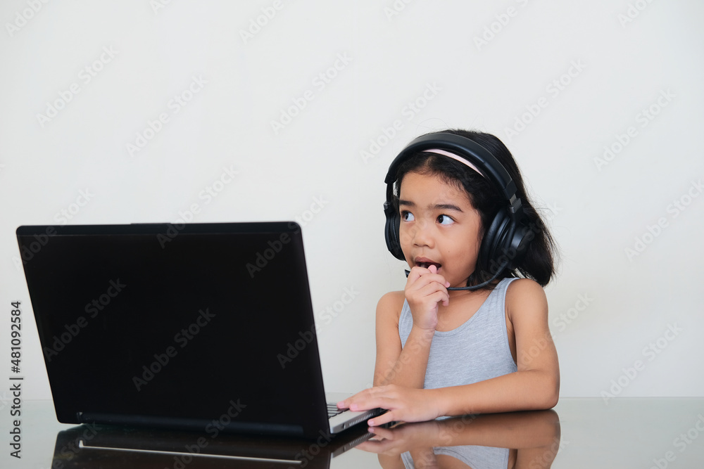 Asian kid talking using headset in front of laptop during her school online class Asian kid talking using headset in front of laptop during her school online class