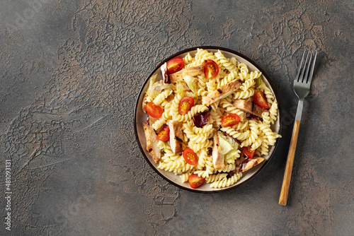Pasta salad with grilled chicken, tomatoes and olive oil in a plate on a dark culinary background. A traditional Italian dish is girandole or fusilli with fried poultry fillet and vegetables. Top view photo
