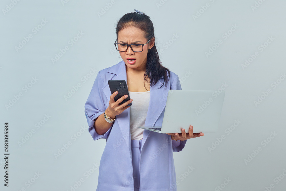 Portrait of angry young Asian woman looking at message on smartphone and holding laptop, knowing canceled job isolated on white background Portrait of angry young Asian woman looking at message on smartphone and holding laptop, knowing canceled job isolated on white background