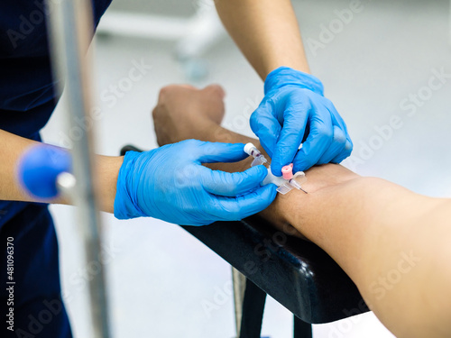 Inserting a catheter needle into a person's arm for intravenous administration of drugs and saline. Selective focus. The doctor's hands in sterile gloves insert the needle into the patient's arm.