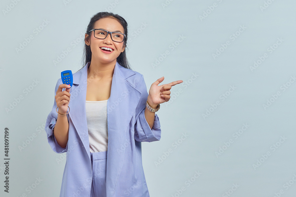 Portrait of cheerful young Asian woman holding banking token and pointing finger at copy space isolated on white background. concept money transfer via internet Portrait of cheerful young Asian woman holding banking token and pointing finger at copy space isolated on white background. concept money transfer via internet