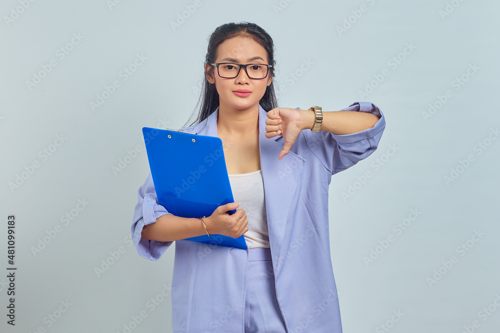 Portrait of annoyed young Asian woman holding document folder and showing thumbs down isolated on purple background Portrait of annoyed young Asian woman holding document folder and showing thumbs down isolated on purple background