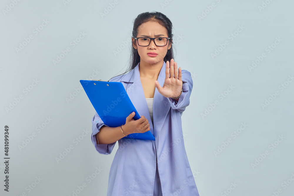 Portrait of angry young Asian woman holding folder and says no shows prohibition gesture refuses something isolated on purple background Portrait of angry young Asian woman holding folder and says no shows prohibition gesture refuses something isolated on purple background