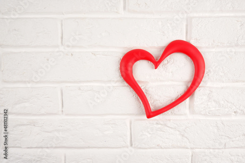 A red heart-shaped frame on a white brick wall. A minimalist design element for happy Valentine's Day, Birthday, Mother's Day and other holidays.The concept of health, kindness, life, a symbol of love