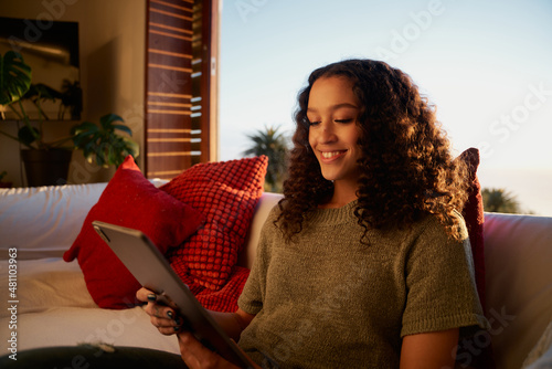 African American female relaxing on sofa scrolling on social media using digital tablet  photo