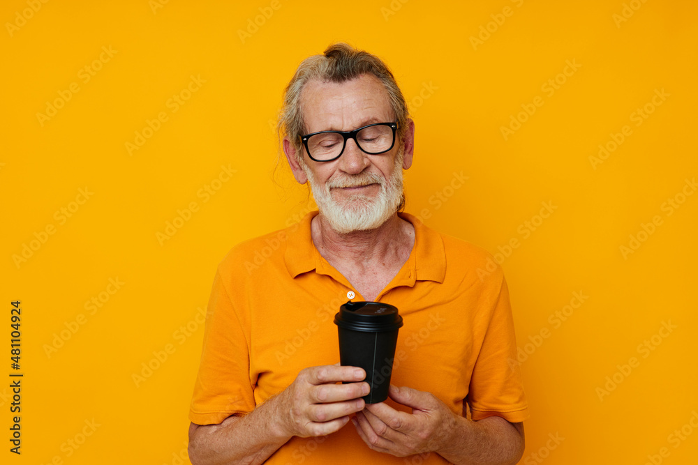 elderly man in a yellow T-shirt a glass with a drink yellow background