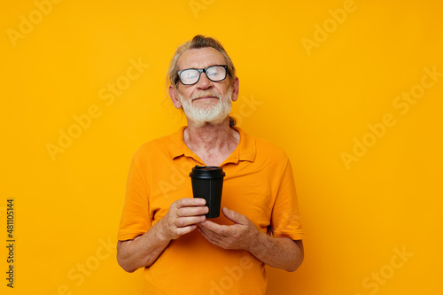Portrait of happy senior man in a yellow T-shirt a glass with a drink cropped view © Tatiana