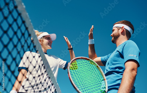 Talent wins games, teamworks wins championships. Low angle shot of two young tennis players giving each other a high five outdoors on the court. © Allistair/peopleimages.com