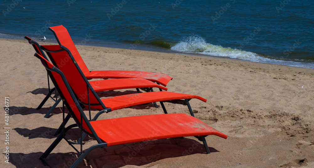 Red sunbeds on the beach. Nobody on the deck chairs. red deck chair on a shallow sandy beach, beach equipment