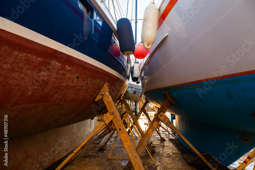 Sailing yachts are in dry dock and supported by metal supports. photo