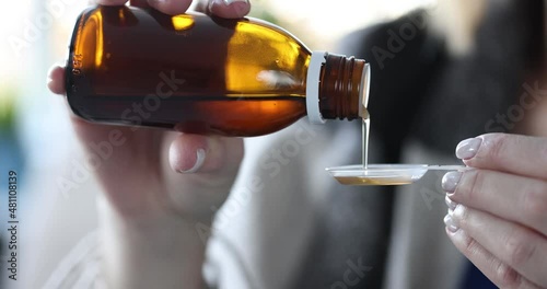 Woman pours cough syrup into measuring spoon photo