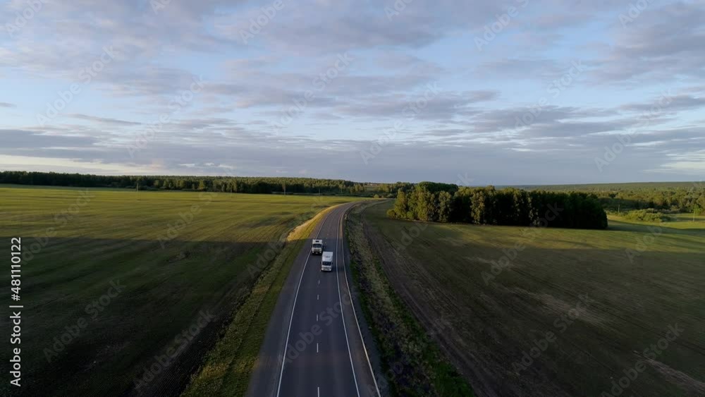 Aerial view of trucks and cars driving on an intercity road between green fields in the beautiful morning of summer day Aerial view of trucks and cars driving on an intercity road between green fields in the beautiful morning of summer day
