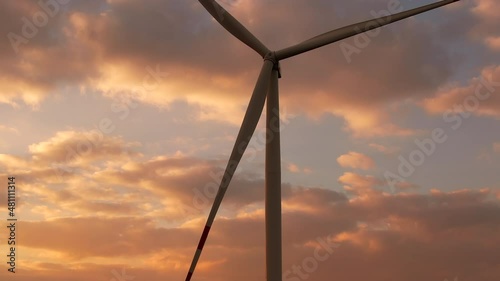 Windmills with huge propellers produce electricity operating at rural station on field at sunset against cloudy sky low angle shot