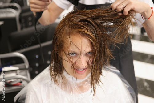 Hairdresser using hairdryer for treatment with hair, dry wet hair after beauty procedure