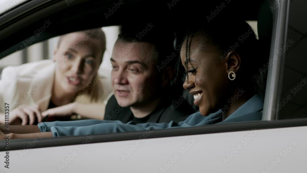 Portrait of a smiling african lady and her european man inspecting the interior of a new car in a modern dealership. An attractive salesperson talks about an electric car and enjoys the beautiful car Portrait of a smiling african lady and her european man inspecting the interior of a new car in a modern dealership. An attractive salesperson talks about an electric car and enjoys the beautiful car