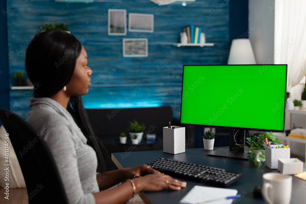 Young adult looking at computer with horizontal green screen, working from home. Entrepreneur using mockup template and isolated background for chroma key on monitor, doing remote work
