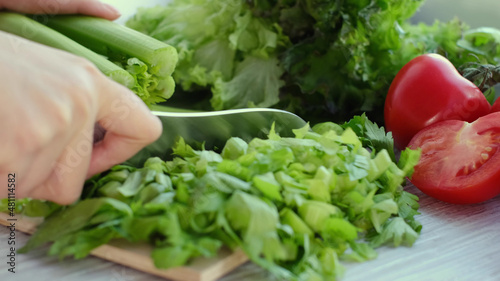 Woman hands using a knife to slice a bunch of fresh celery. Food fresh stalks of Celery peeling. Culinary delicious food being prepared.