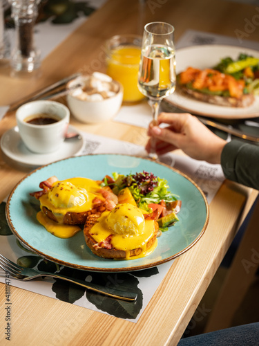 Top view breakfast - eggs Benedict with hollandaise cheese sauce, toast and fresh salad served on plate in restaurant or cafe interior background. Close up, selective focus