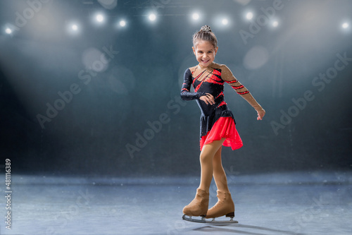 Little skater rides on rings in red and black dress on ice arena photo