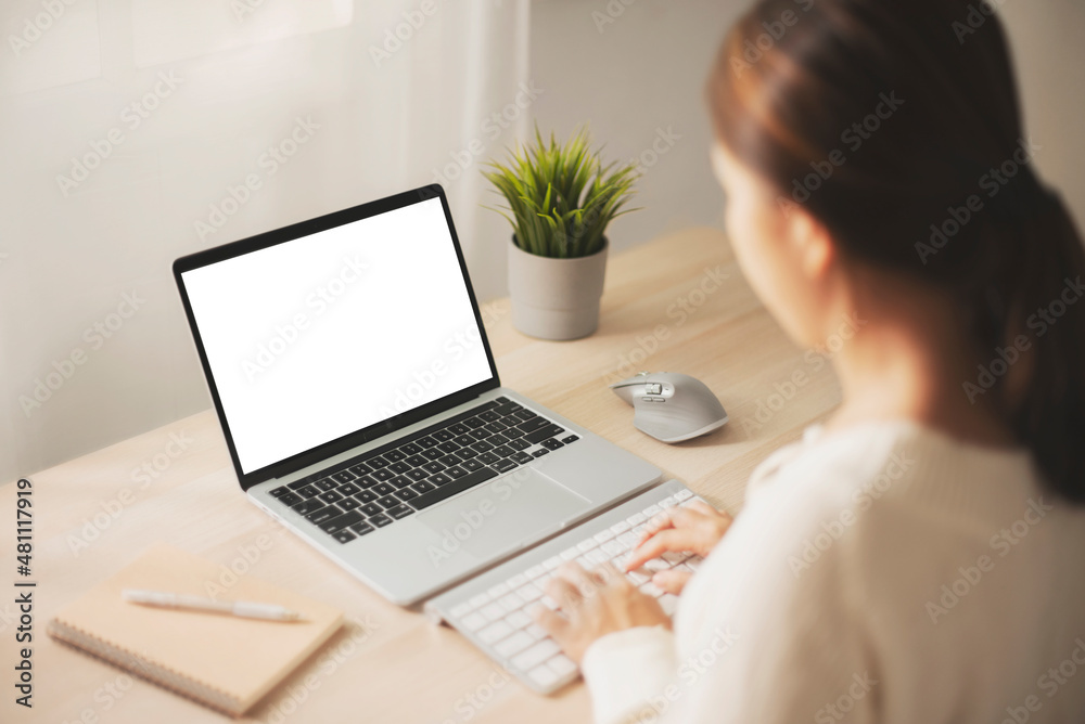 Fototapeta premium Women using laptop with blank screen at table in the office, Back view of business women hands busy using laptop at office desk.