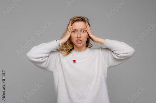 Scared, shocked, worried woman, grab head, gasping and drop jaw, shivering from fear, watching horror movie, standing terrified, wears white sweater, gray background