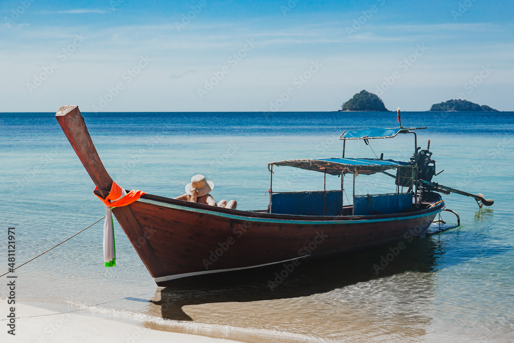 Unidentified woman sitting on a wooden boat in the sea sun bathing.
